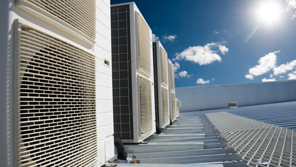 Air conditioner units on a roof of industrial building with blue sky and clouds in the background.